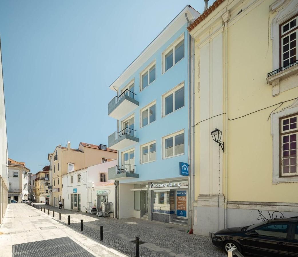 Street view of buildings with a bright blue facade and balconies, located on a sunny day.